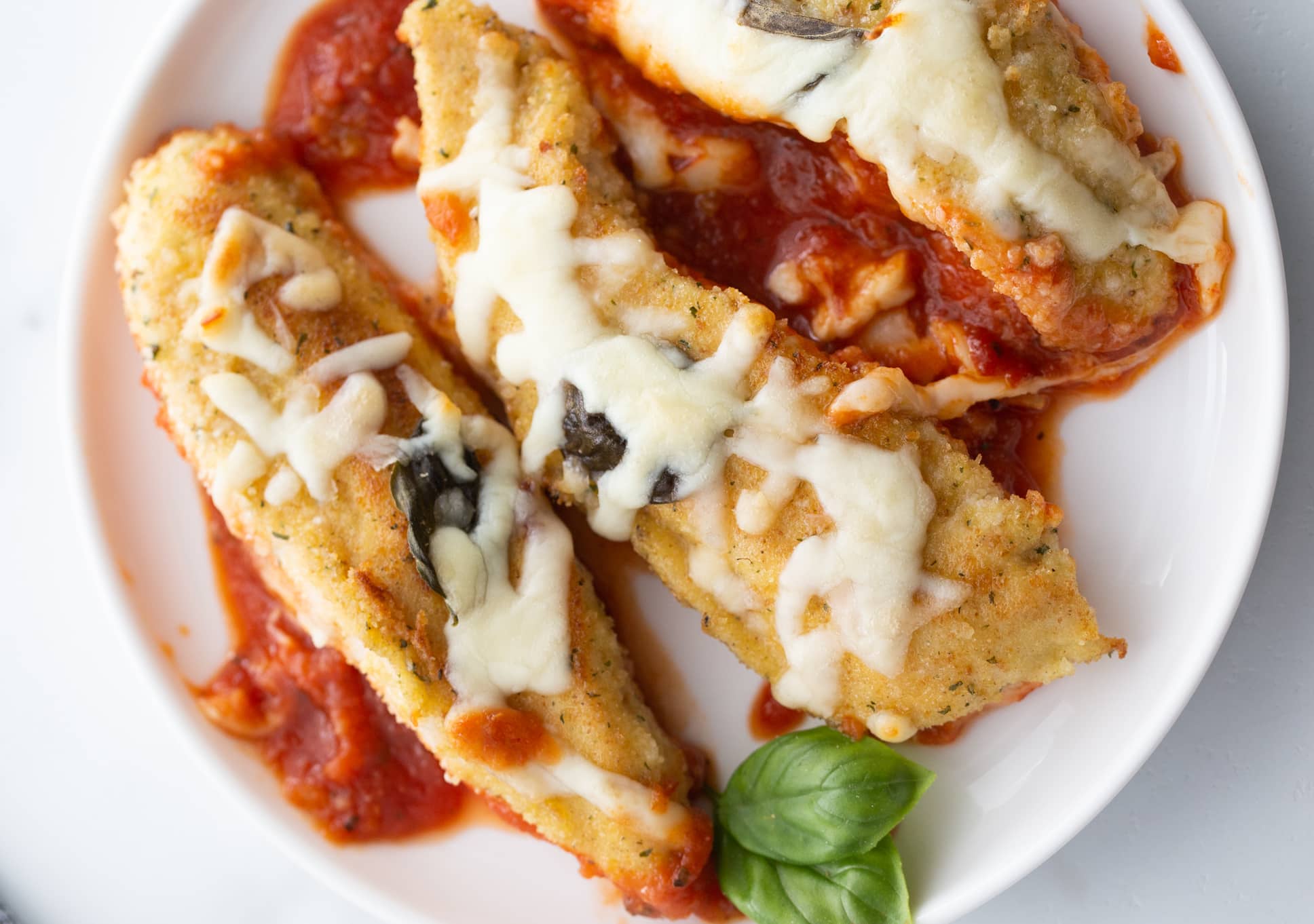 Plated chicken tenderloin with marinara and cheese A serving of chicken tenderloin marinara bake on a white plate with extra sauce