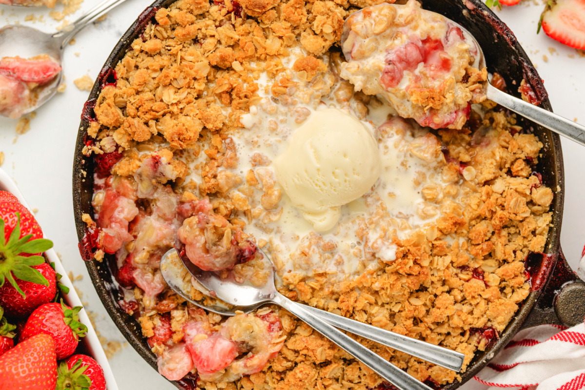 Strawberry banana crisp with oat topping and ice cream Close-up of baked strawberry banana crisp in cast iron skillet with melted vanilla ice cream.