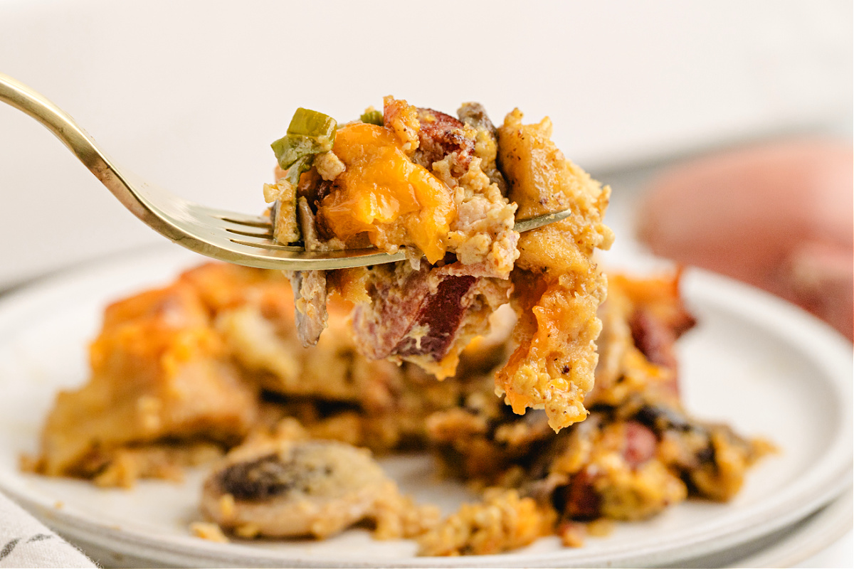 Cheesy bagel breakfast casserole with smoky kielbasa. Fork lifting a cheesy bite of bagel breakfast casserole with kielbasa.