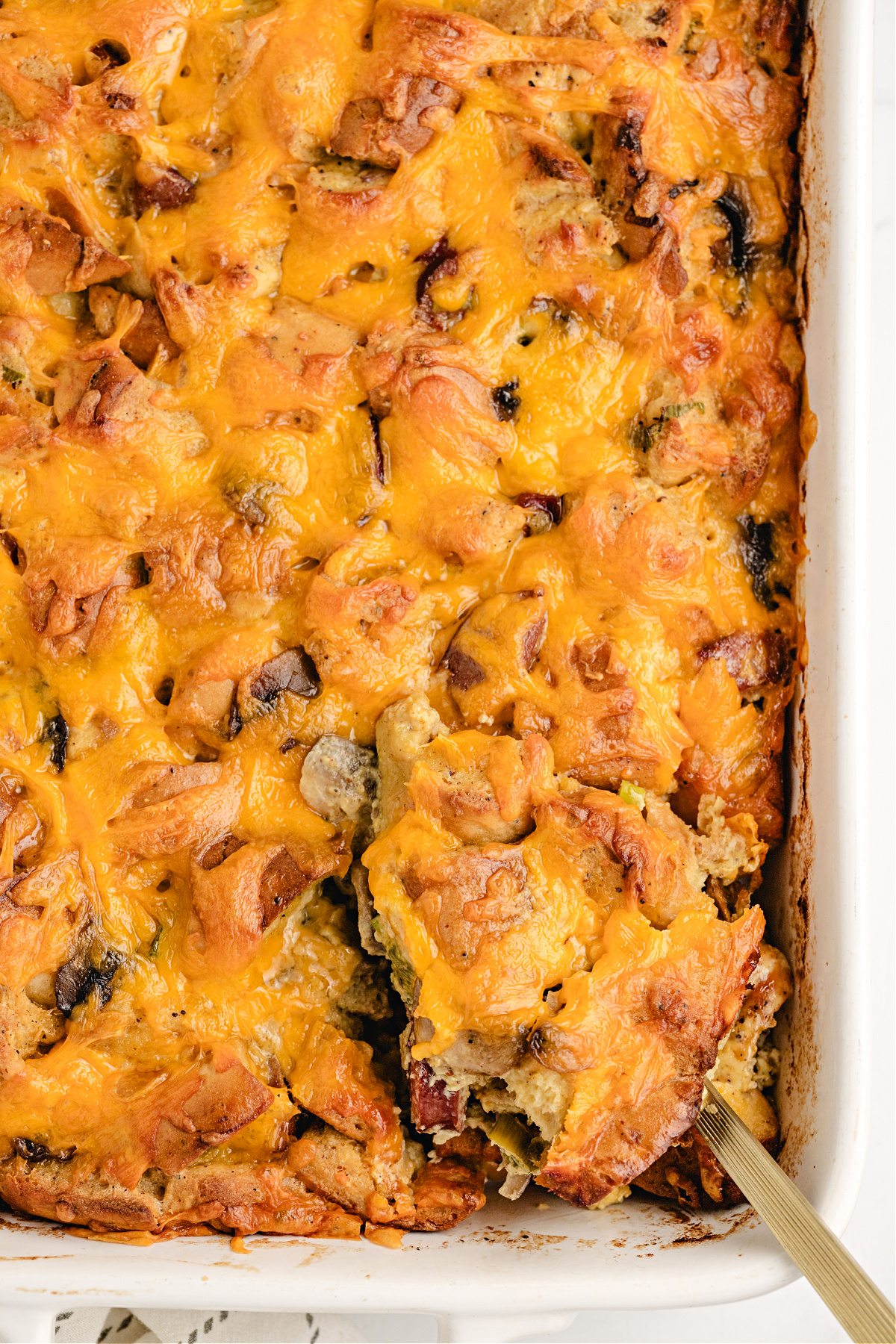 Cheesy breakfast casserole baked with bagels and kielbasa. Golden cheesy breakfast casserole in a white baking dish with kielbasa.