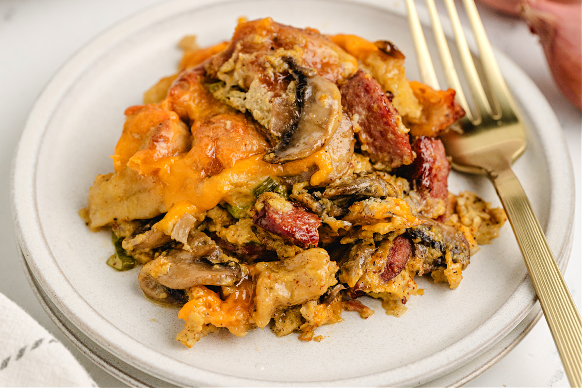 Serving of bagel breakfast casserole with smoky kielbasa. Plate of cheesy egg casserole with kielbasa, mushrooms, and bagel cubes.