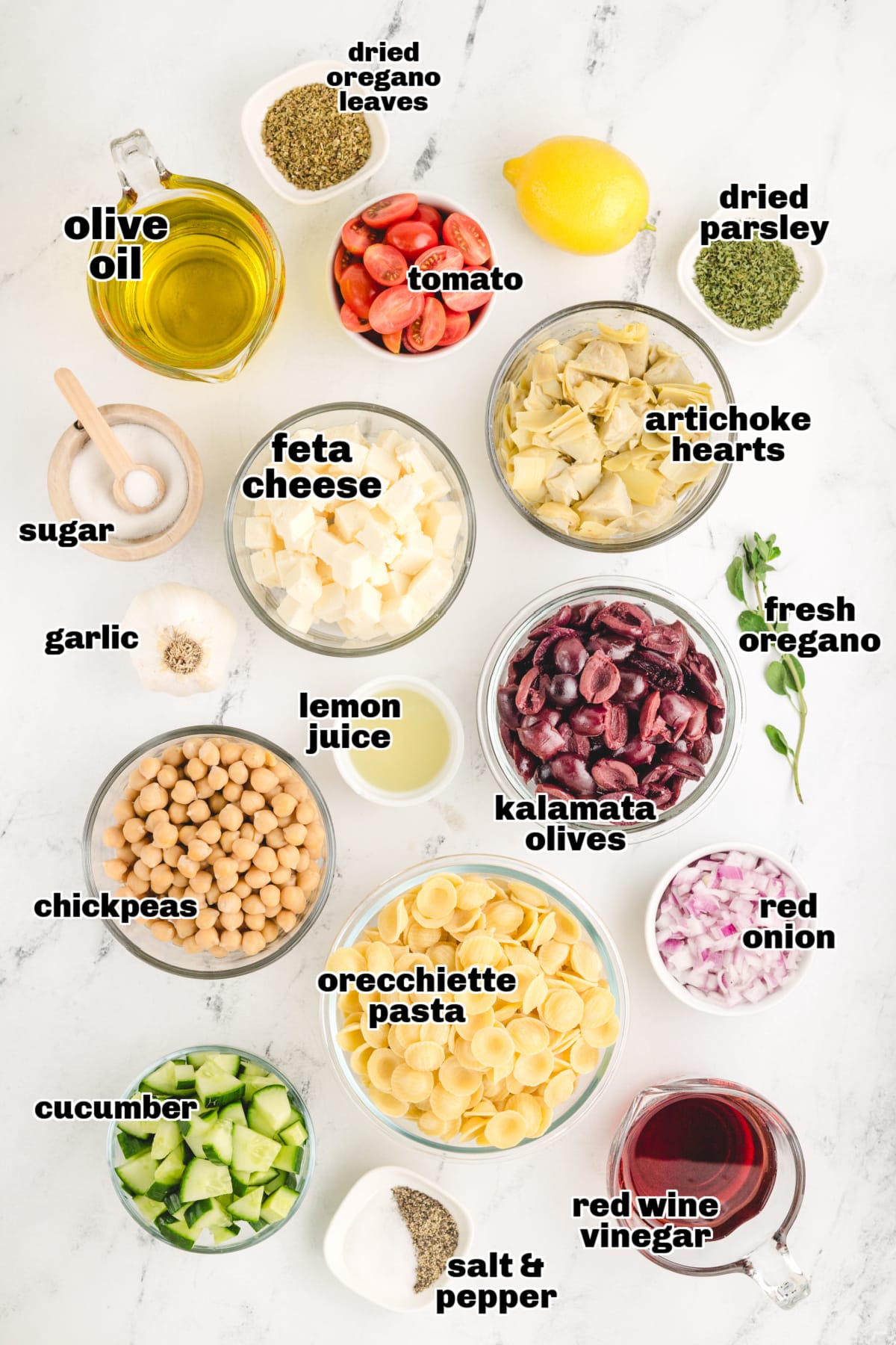 All the ingredients laid out on a countertop, including pasta, feta, olives, cucumbers, and dressing components.