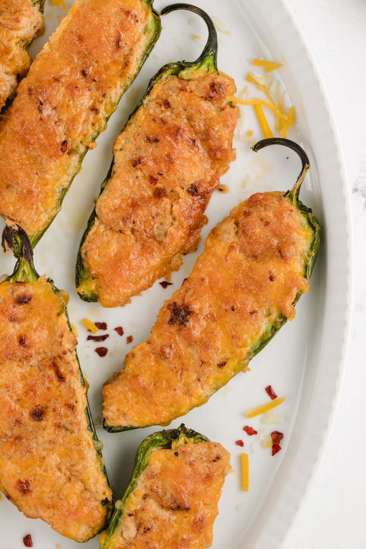 Close-up of baked ground turkey stuffed jalapeños on a baking sheet, topped with melted cheese and golden edges.