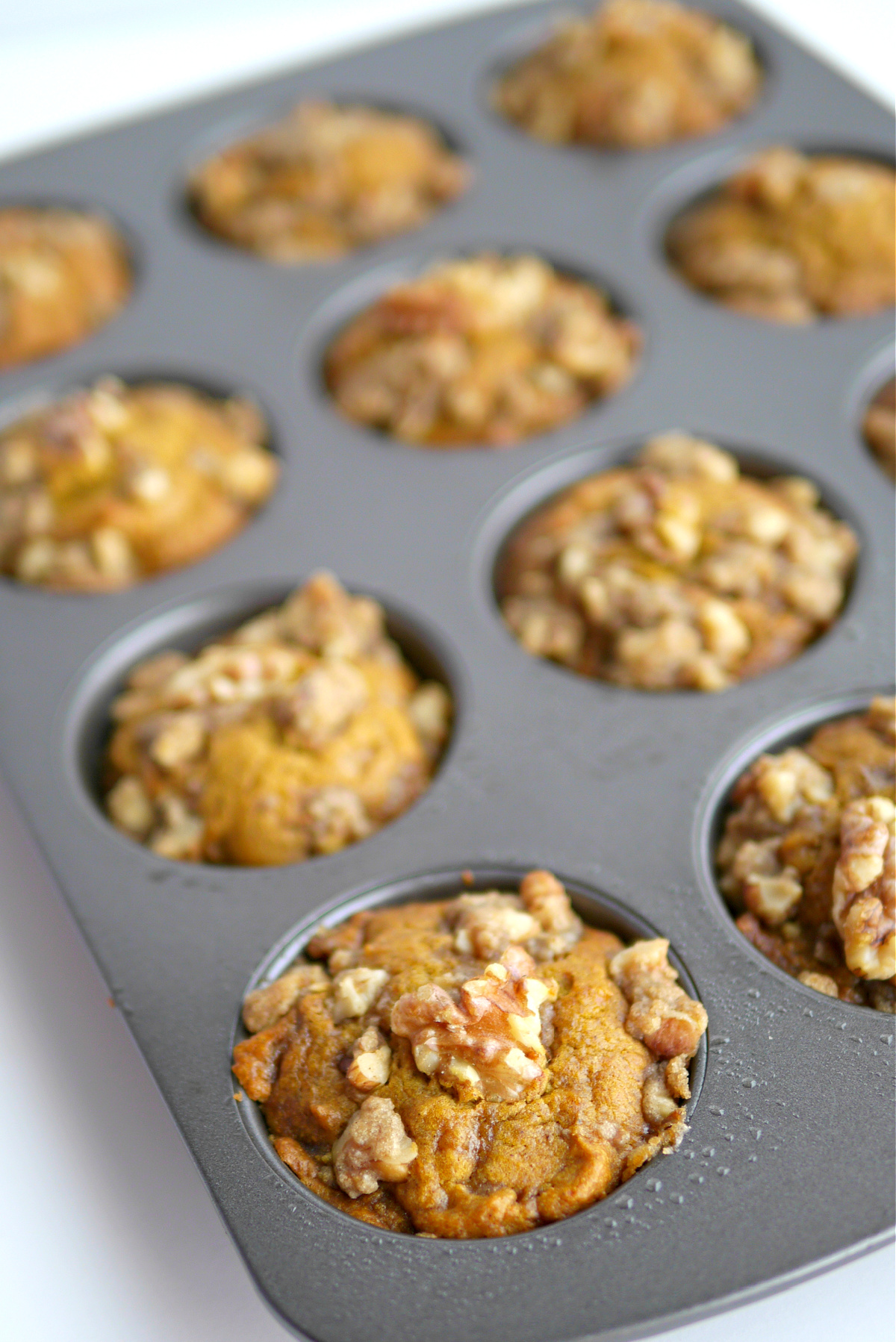 Pumpkin brown sugar muffins fresh out of the oven in a muffin tin with walnut crumble tops.