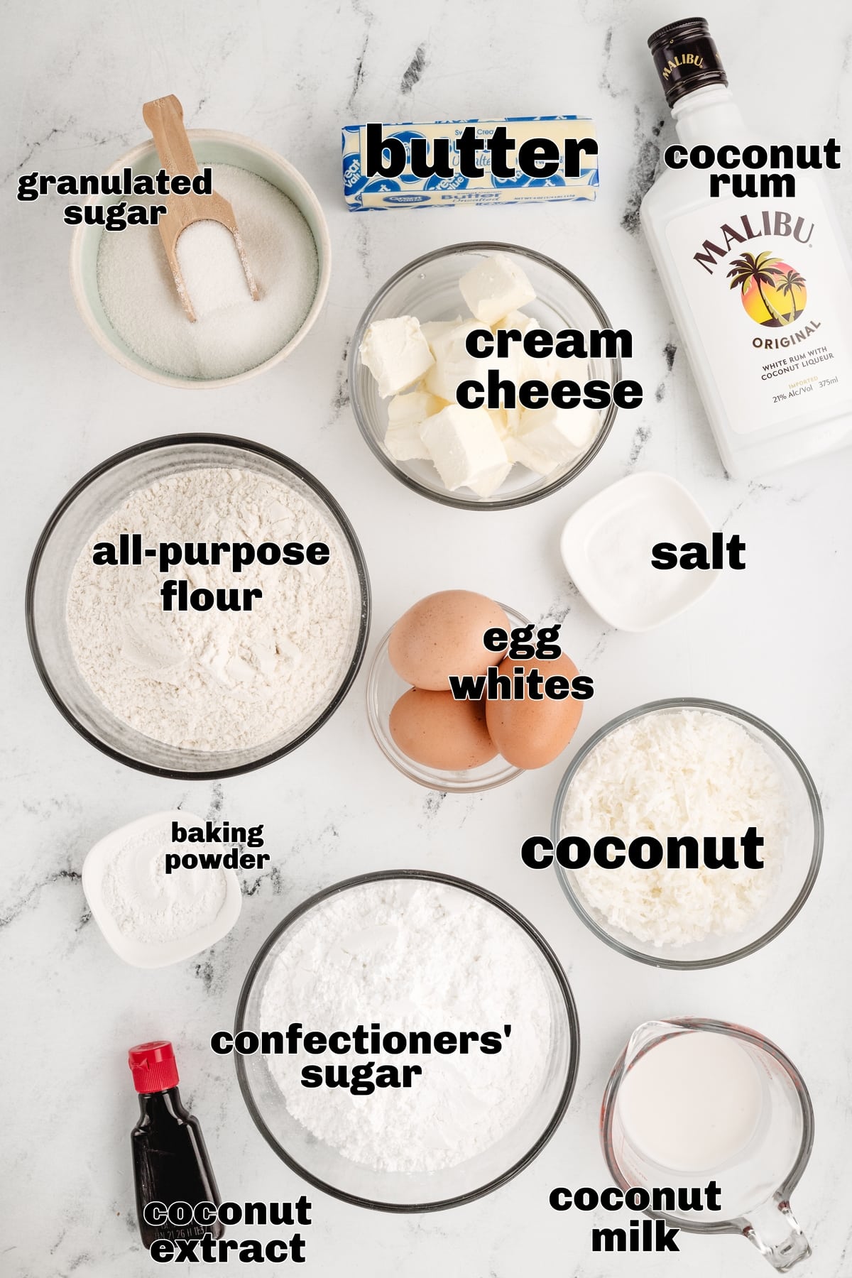 Ingredients including coconut milk, shredded coconut, coconut rum, and coconut extract laid out on a kitchen counter.