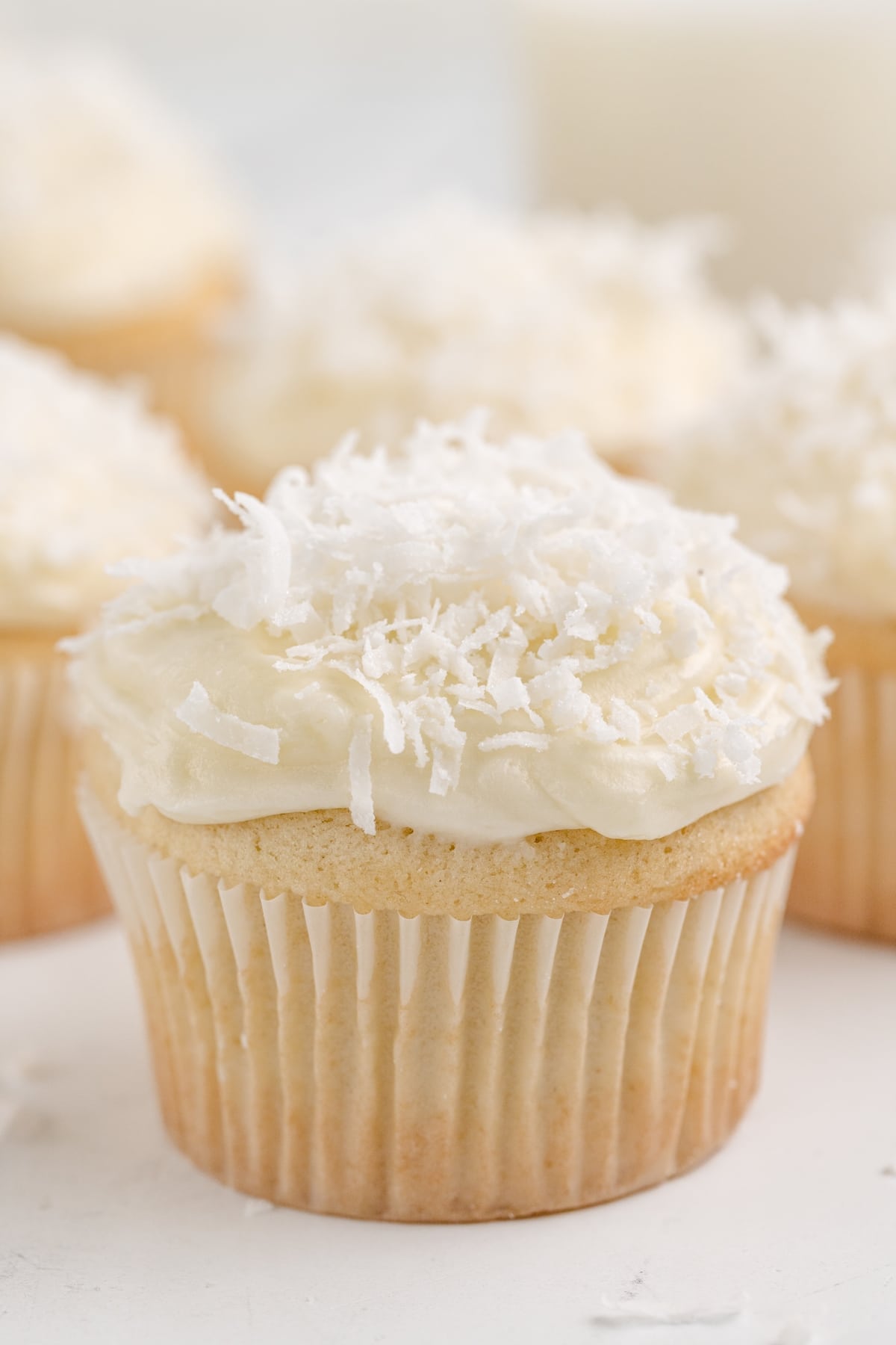 Coconut cupcakes with a soft, moist texture and a coconut cream cheese frosting swirl, garnished with coconut flakes.