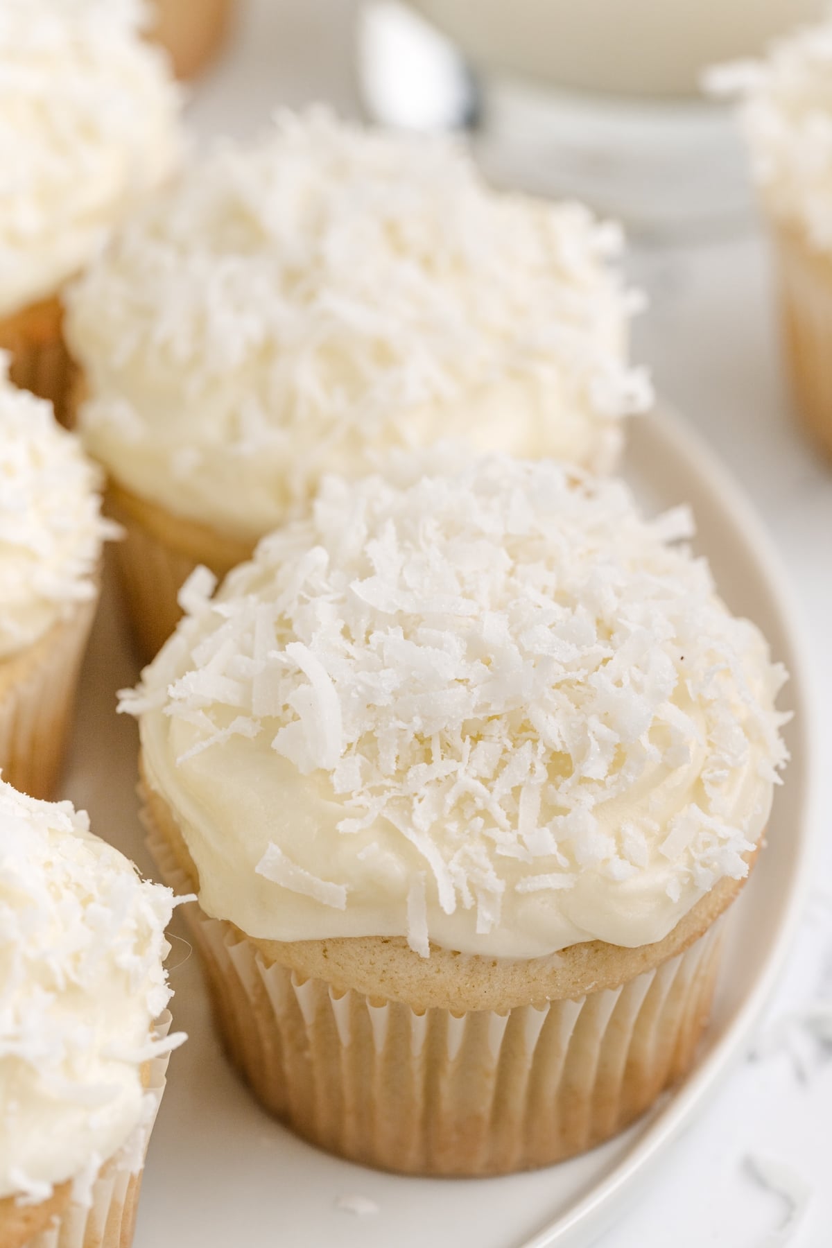 Coconut cupcakes with a soft, moist texture and a coconut cream cheese frosting swirl, garnished with coconut flakes.