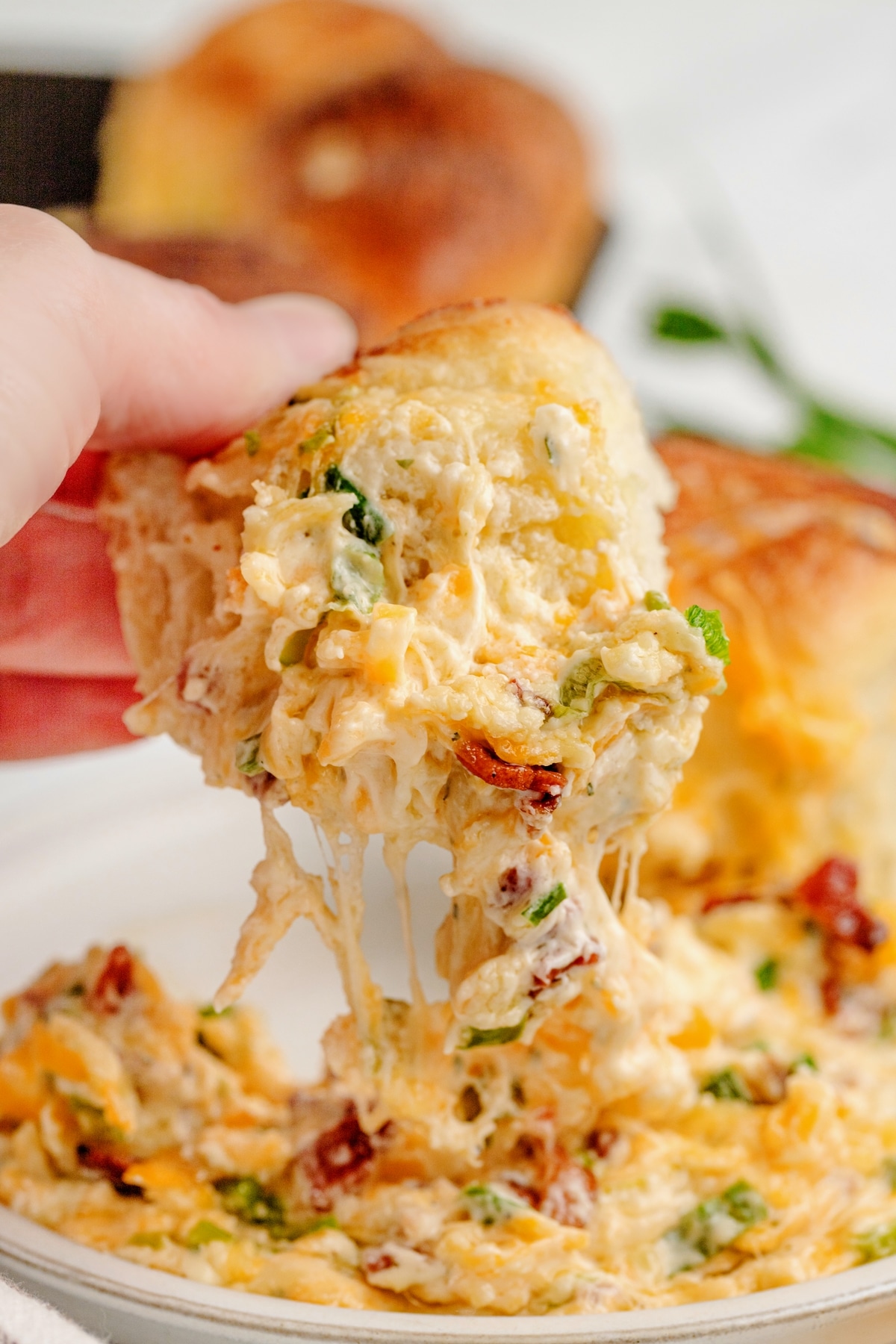 Hand scooping a serving of sour cream bacon ranch dip from the center of a ring of golden-brown dinner rolls.