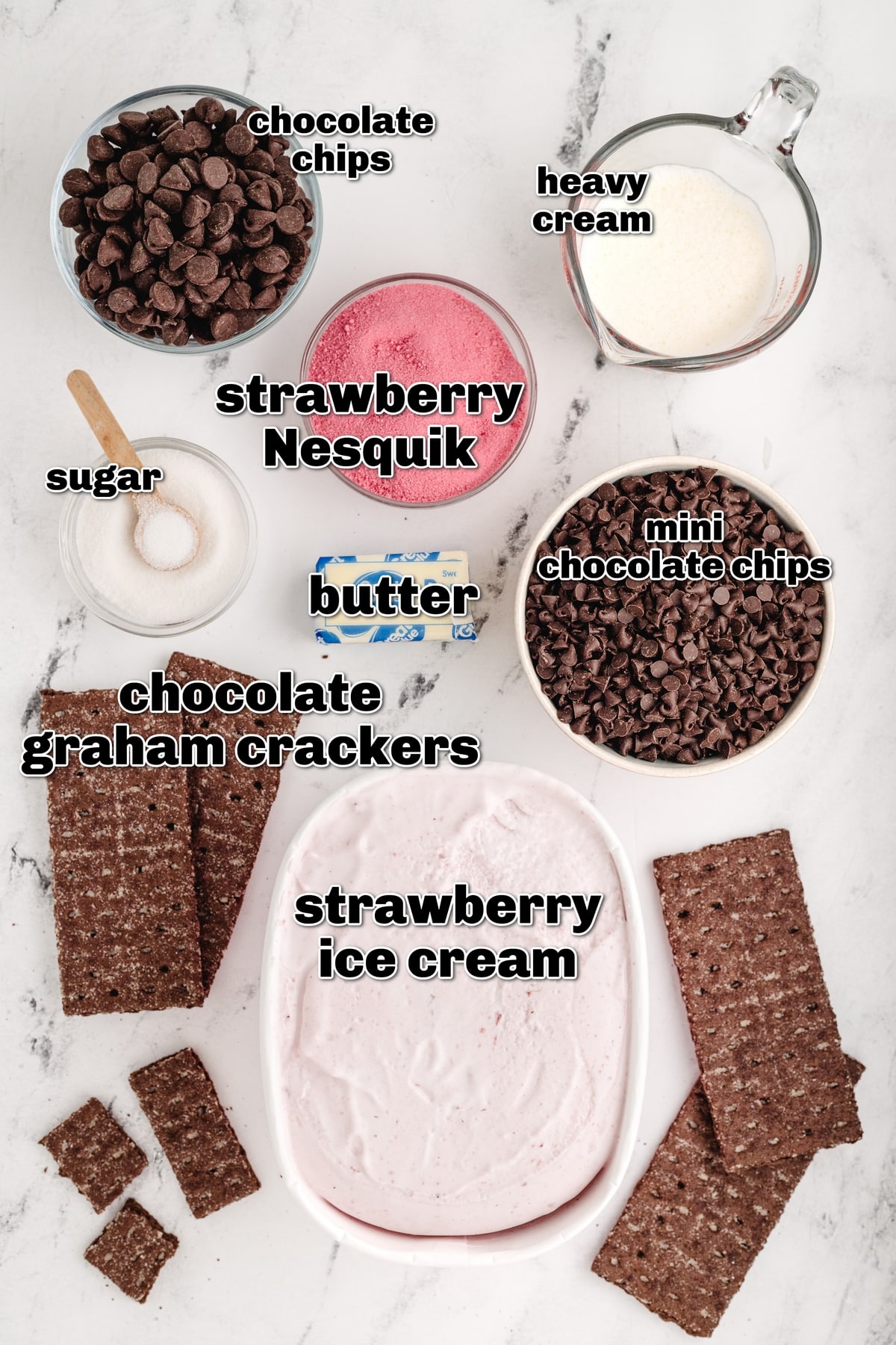 A flat lay of all the ingredients including chocolate graham crackers, strawberry ice cream, mini chocolate chips, strawberry milk powder, heavy cream, and semi-sweet chocolate chips.