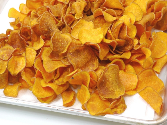 A pile of the Best Homemade Sweet Potato Chips on a baking tray.