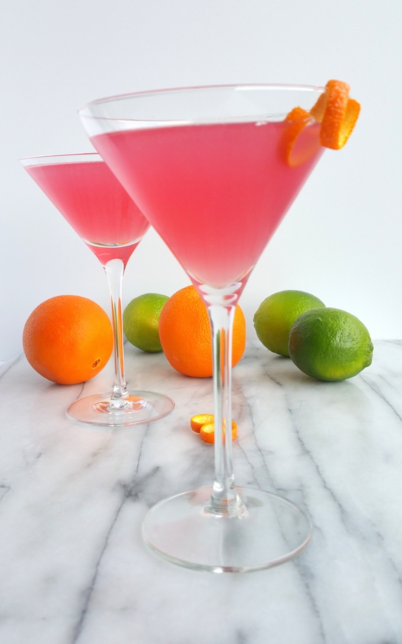 World's Best Cosmopolitan Cocktail in martini glasses with limes and oranges in the background.