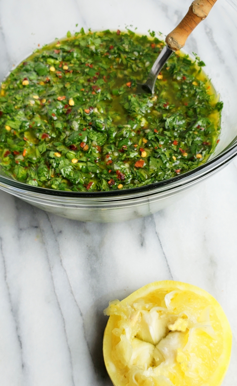 Make the best street food at home with these Flank Steak Tacos with Garlicky Cilantro Chimichurri. These tacos are essentially going to be your go-to summer, grilling meal. #noblepig #grilling #beef #flanksteak #chimichurri Chimichurri in a bowl with a spoon and a squeezed half of a lemon.