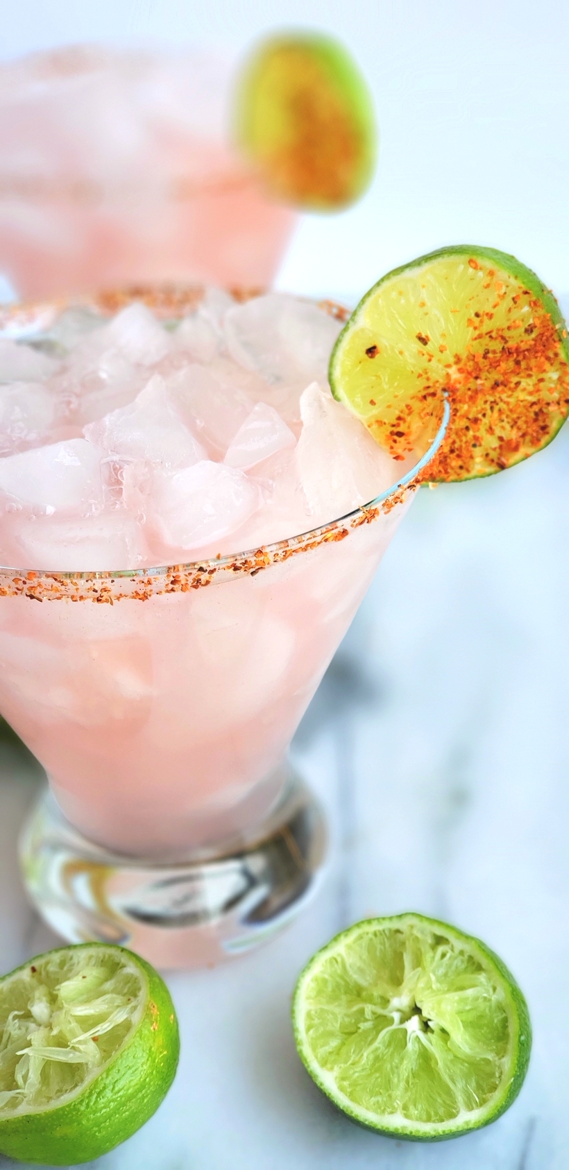 The petal pink color of this Icy Hibiscus Margarita is alluring, but it's the sweet, tangy and refreshing flavor that will have you asking for a second pour. #cocktail #noblepig Two margaritas with limes squeezed around them.