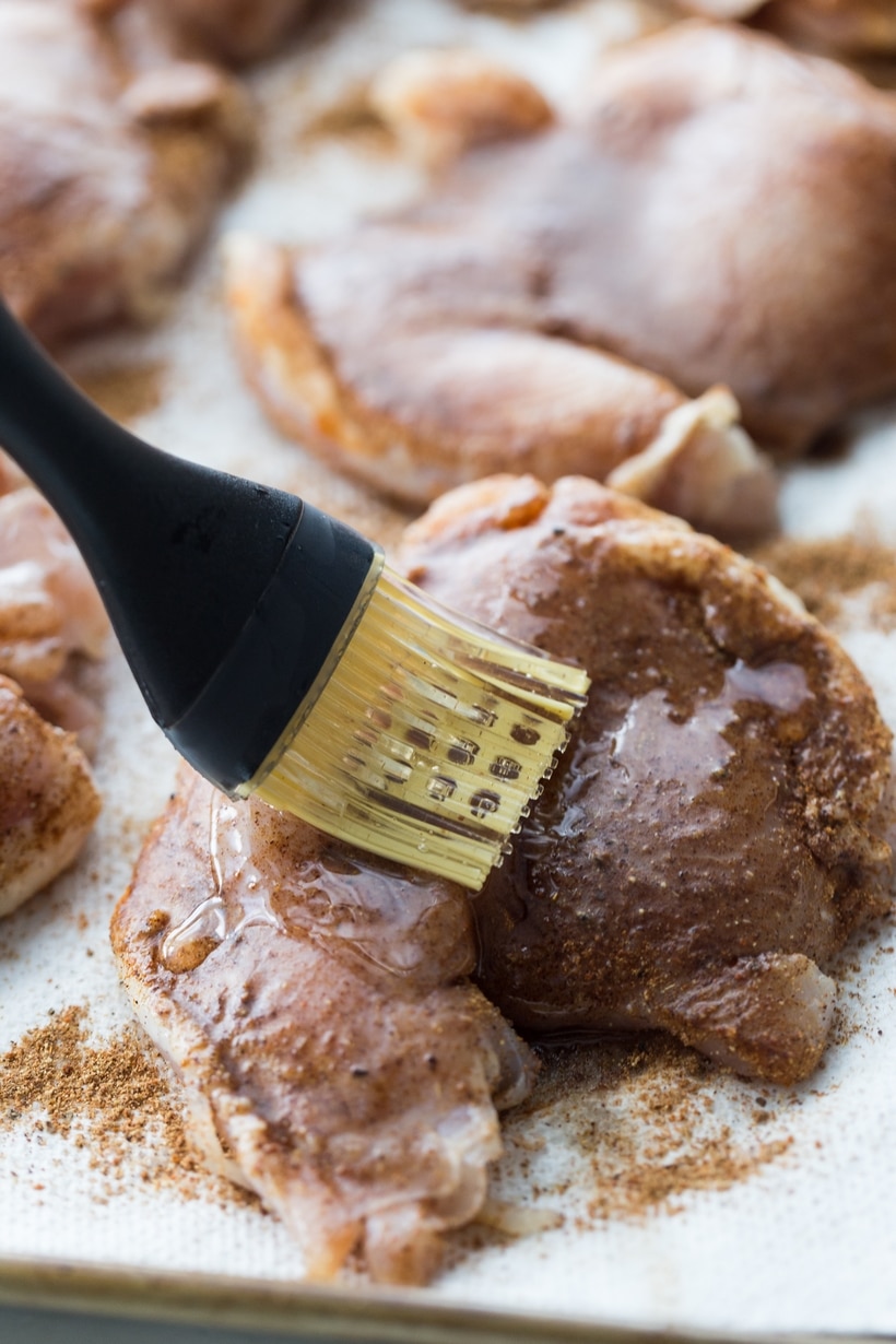 Air Fryer Caribbean Spiced Chicken A pastry brush applying melted coconut oil to the spiced chicken thighs before air frying.