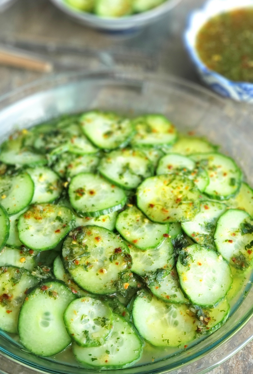 Keep it light and refreshing ~ Cucumbers with Mint Vinaigrette are the perfect side dish for any meal. They are especially wonderful with Asian Cuisine. #cucumbers #sidedish #asiancuisine Sliced cucumbers in a large bowl with vinaigrette on top.
