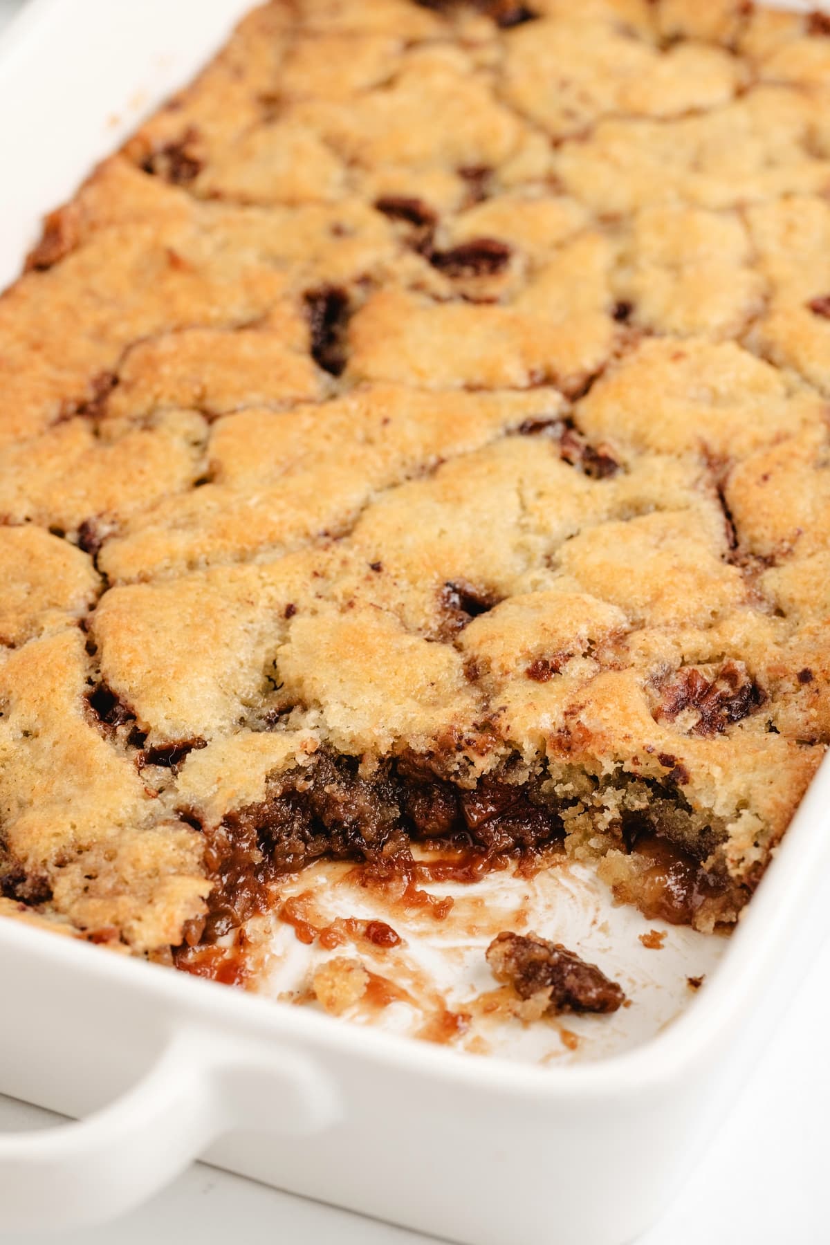 Pecan Pie Cobbler with a Serving Removed Pecan Pie Cobbler in a baking dish with a serving scooped out, revealing its rich, nutty interior.
