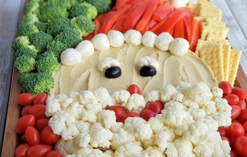 This Santa Snack Board is the perfect holiday centerpiece for every gathering this season. Not only is this healthy snack board festive and fun, it uses simple ingredients everyone loves. This Santa Board transports easily, feel free to take it along to every celebration this season. #noblepig #santasnackboard #diysantasnackboard #diy #healthysnackboard #christmas #christmasrecipes #easychristmasrecipes #holidayrecipes #santafood #santa #holidayentertaining #holidayfood #christmasappetizer Santa's face made with various vegeatables.