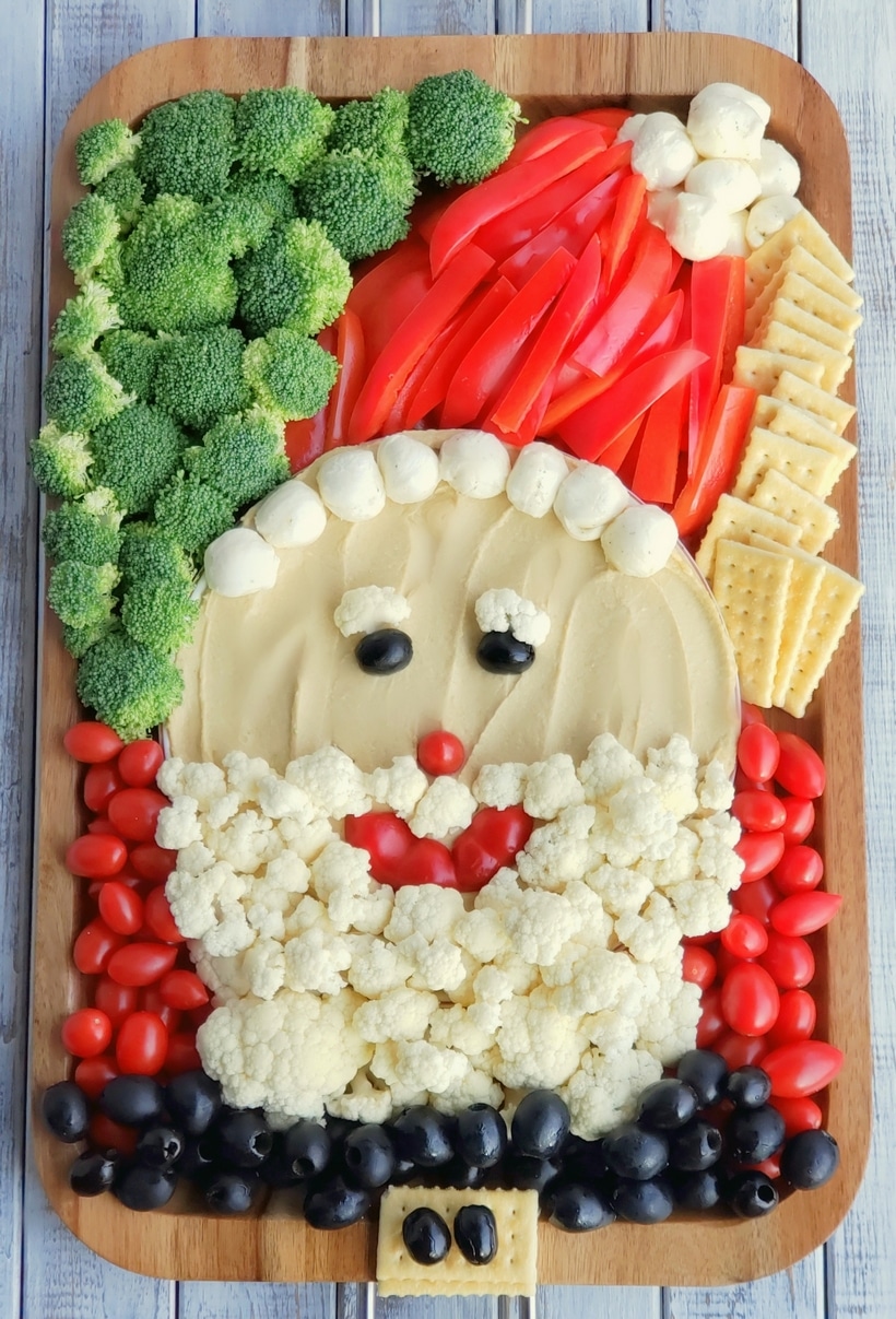 This Santa Snack Board is the perfect holiday centerpiece for every gathering this season. Not only is this healthy snack board festive and fun, it uses simple ingredients everyone loves. This Santa Board transports easily, feel free to take it along to every celebration this season. #noblepig #santasnackboard #diysantasnackboard #diy #healthysnackboard #christmas #christmasrecipes #easychristmasrecipes #holidayrecipes #santafood #santa #holidayentertaining #holidayfood #christmasappetizer Santa Snack Board made with various vegetables and crackers to look like santa.