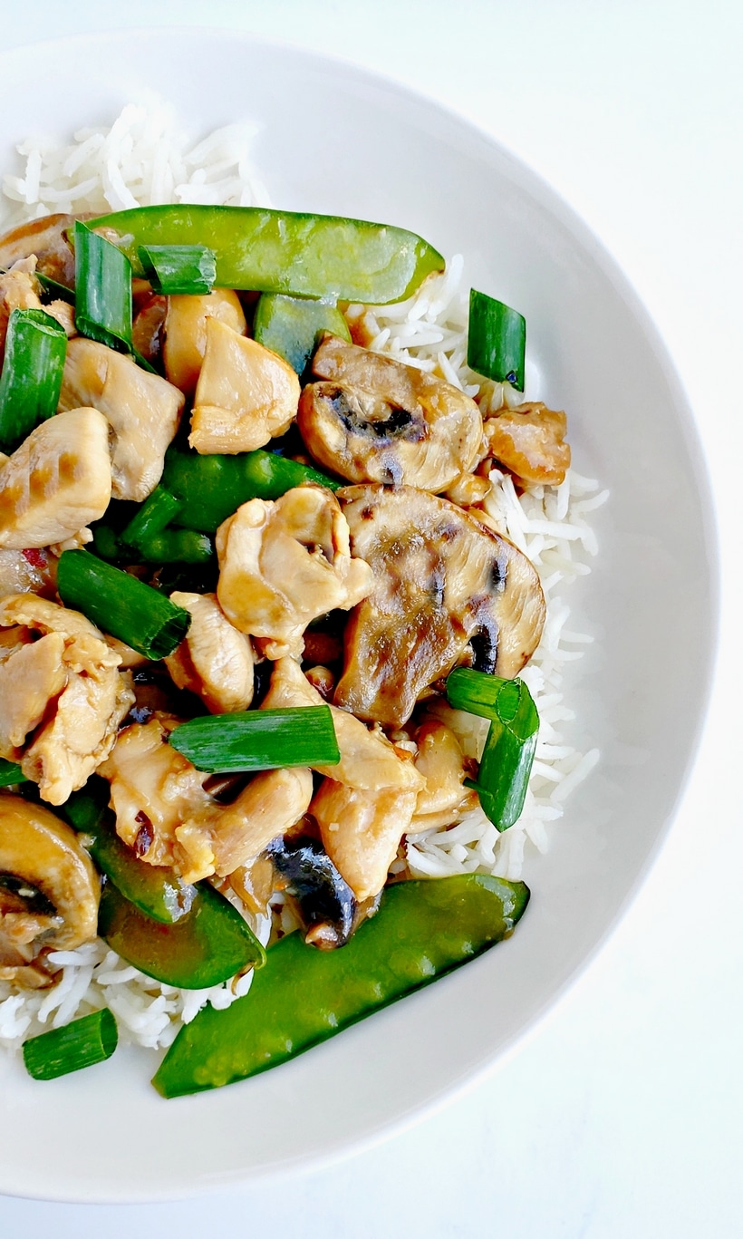 Close up of chicken and snow pea stir fry on a white plate.