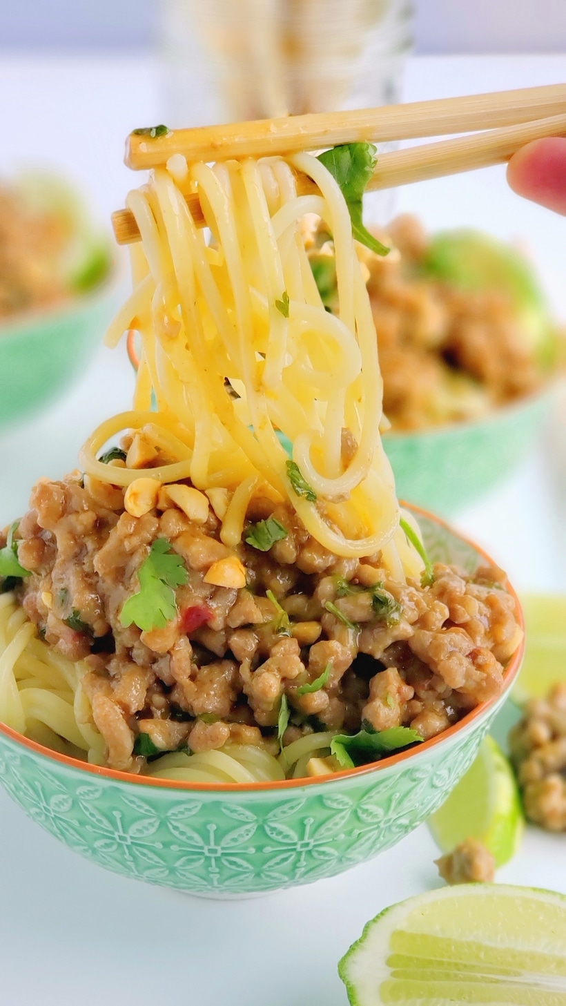 Chopsticks lifting dan dan noodles out of a bowl.