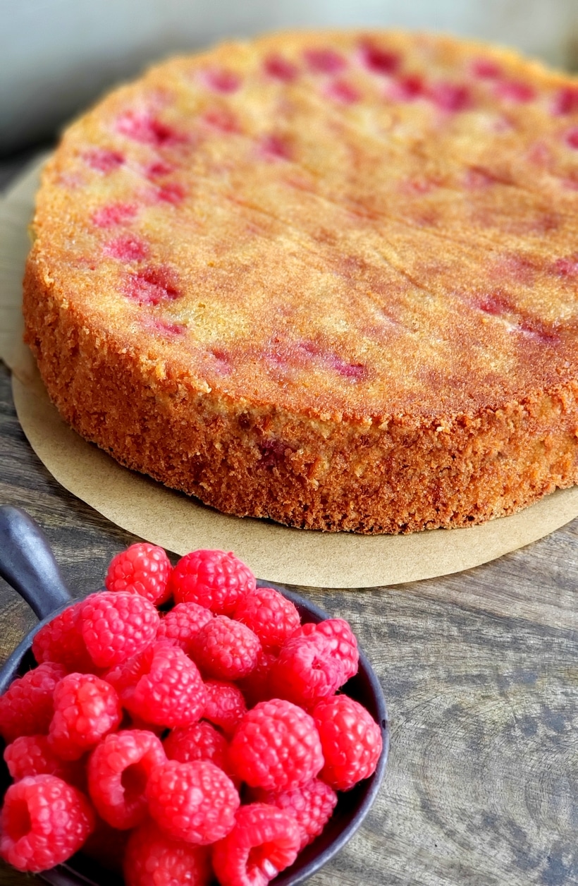 Fresh raspberries in a bowl and a the whole cake in the background.