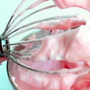 Whipping attachment lifting out strawberry mousse out of a bowl.