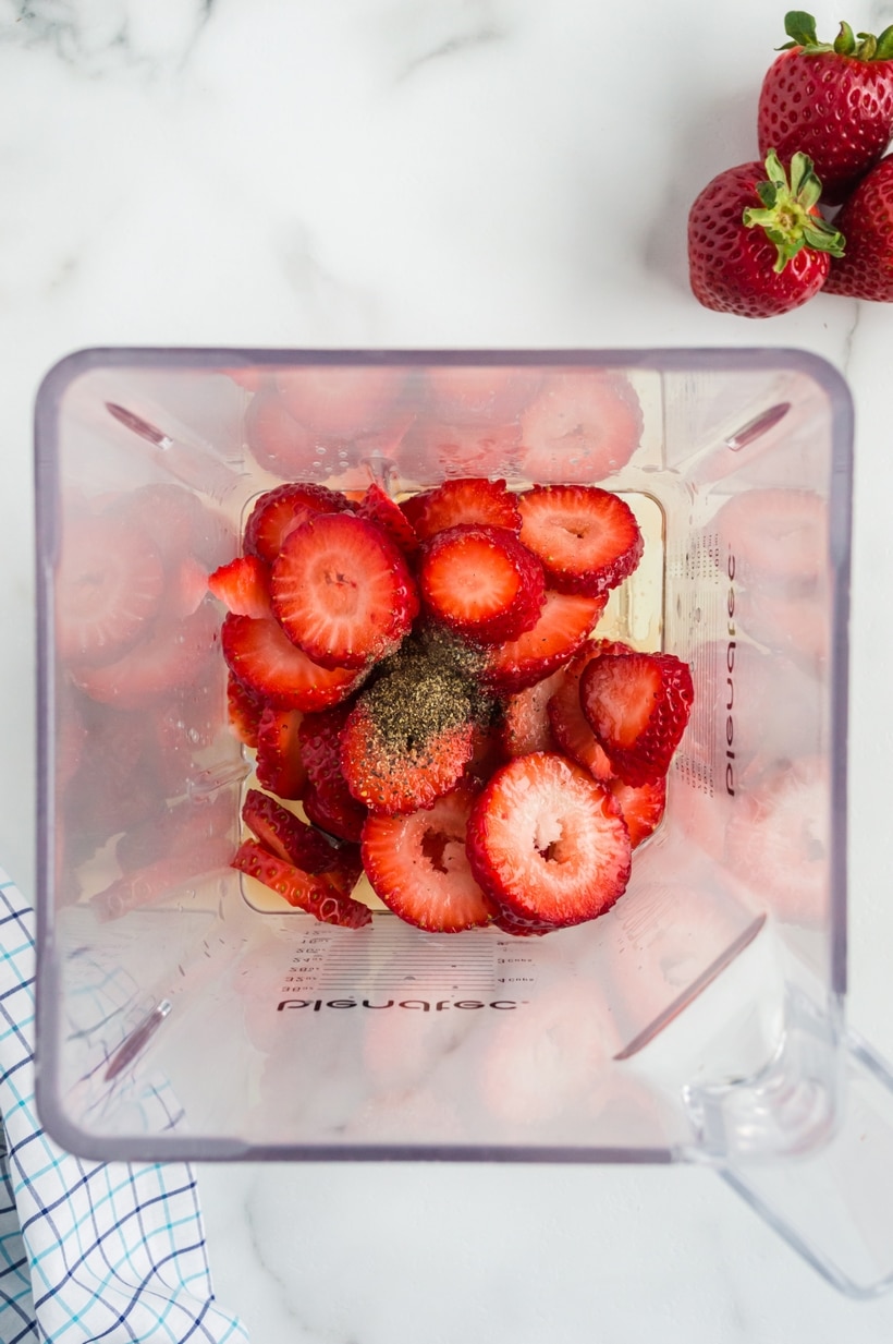 Strawberry Spinach Salad with Strawberry Vinaigrette with fresh strawberries Overhead shot of an open-top blender filled with strawberries, black pepper, and other vinaigrette ingredients, ready to be blended.