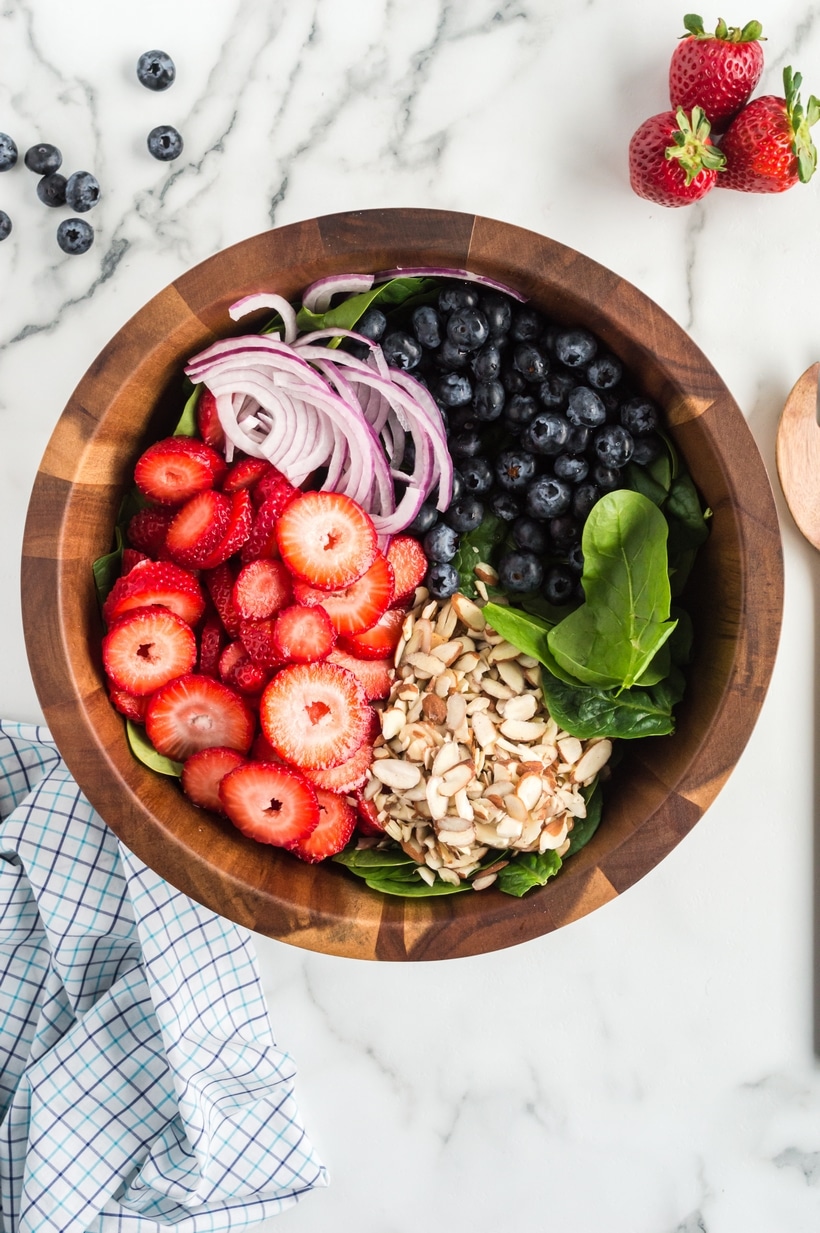Strawberry Spinach Salad with Strawberry Vinaigrette in a bowl Large bowl filled with fresh spinach, sliced strawberries, red onion, and almonds, not yet tossed, showing the individual salad ingredients.