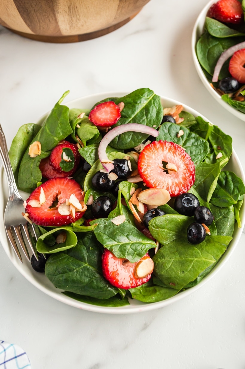 Strawberry Spinach Salad with Strawberry Vinaigrette fresh A served bowl of Strawberry Spinach Salad with a fork, ready to eat, with fresh ingredients and dressing evenly distributed.