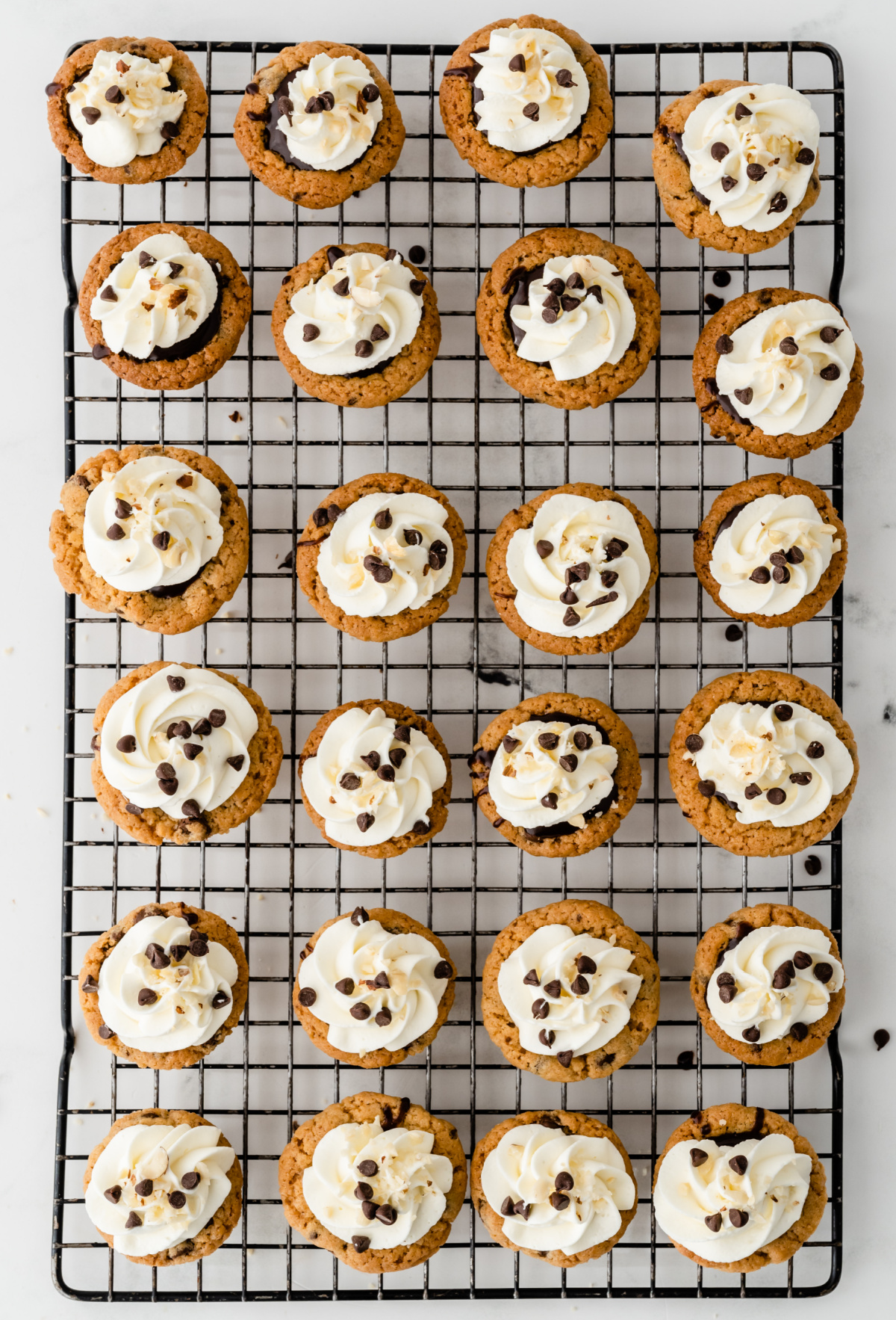 Mini muffin tin cookie cups filled with Nutella chocolate filling and finished with whipped cream Chocolate chip cookie cups with Nutella filling and whipped cream arranged on a cooling rack