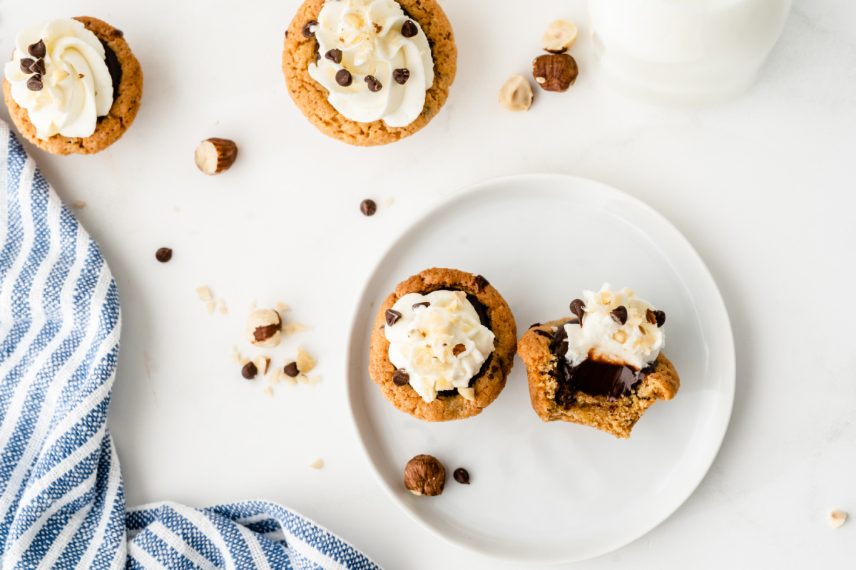 Nutella chocolate cookie cups baked in a mini muffin tin with a soft cookie shell and creamy Nutella center Nutella chocolate cookie cups topped with whipped cream and chocolate chips on a white plate