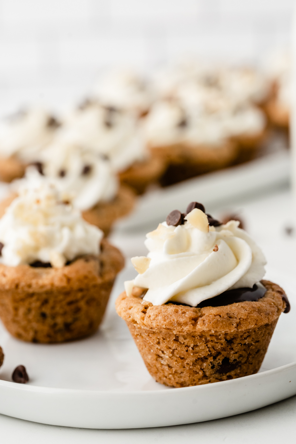 Bite-sized Nutella chocolate cookie cups baked in a mini muffin tin and finished with whipped cream and chocolate chips Nutella chocolate cookie cups topped with whipped cream and chocolate chips on a serving platter
