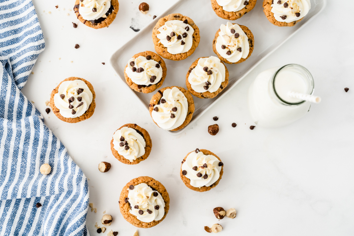 Overhead view of Nutella chocolate cookie cups baked in a mini muffin tin and topped with whipped cream Nutella chocolate cookie cups arranged on a tray with whipped cream and chocolate chips