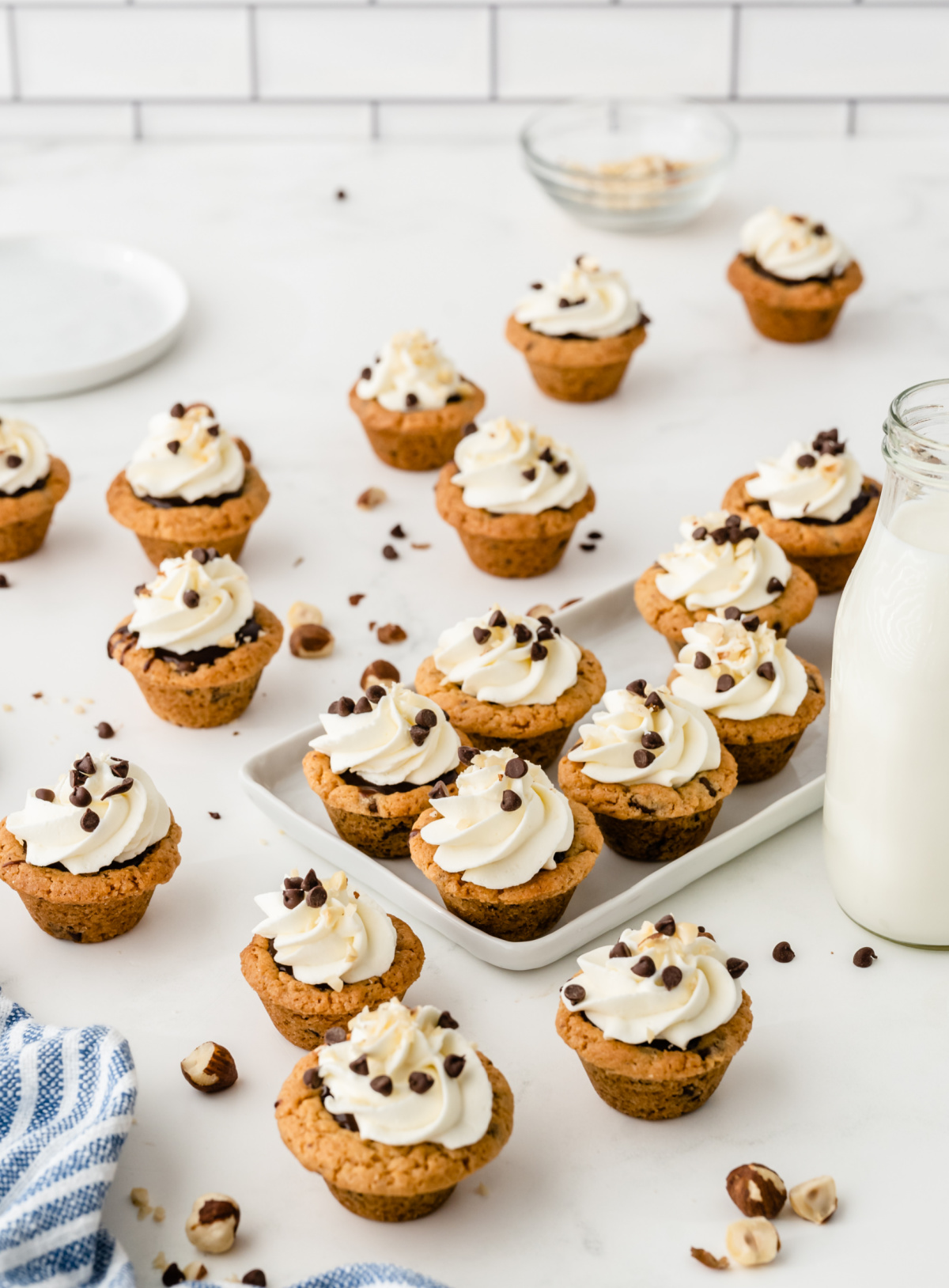 Nutella chocolate cookie cups arranged on a platter with whipped cream, chocolate chips, and hazelnuts Nutella chocolate cookie cups topped with whipped cream and mini chocolate chips on a serving platter