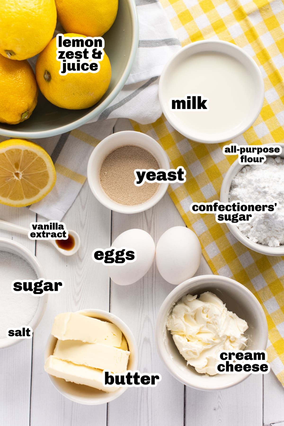 A flat lay of ingredients for lemon buns, including flour, sugar, butter, eggs, milk, yeast, and fresh lemons.