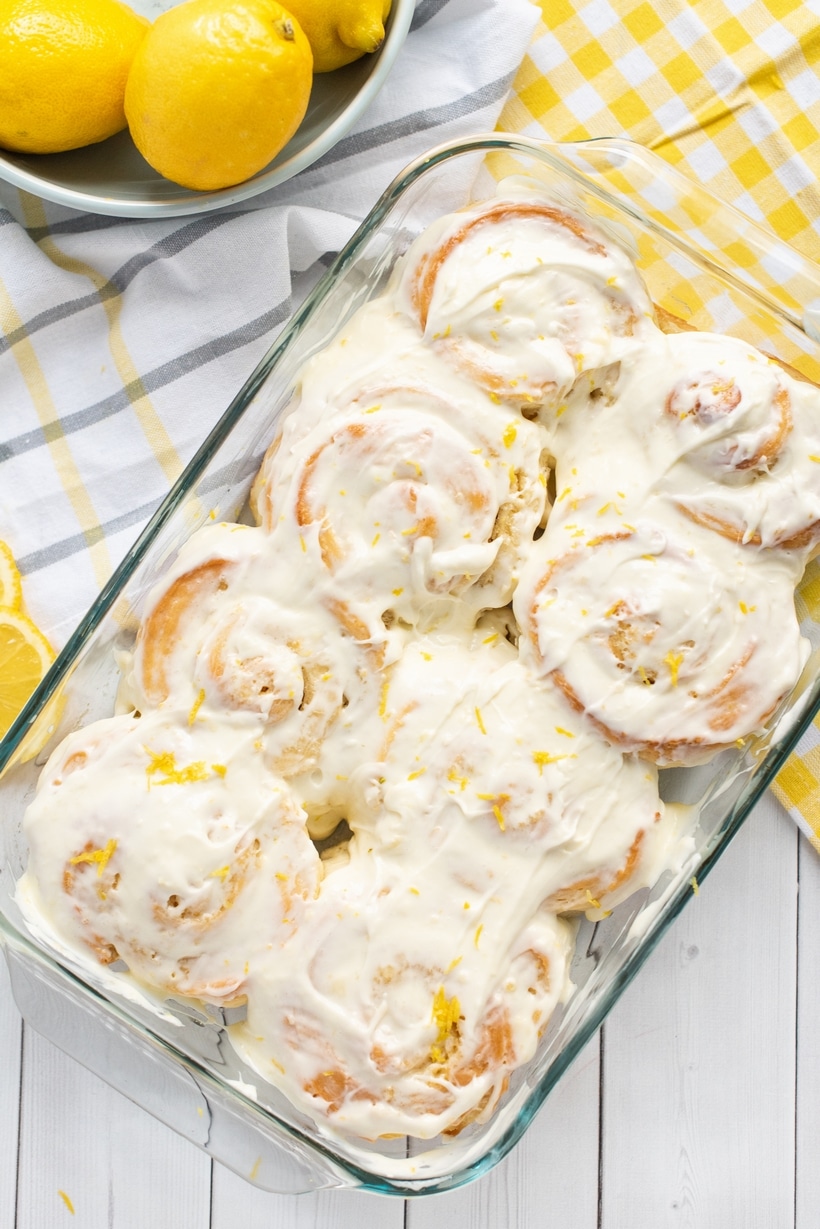 A close-up top view of warm lemon buns in a baking dish, covered in smooth cream cheese icing.