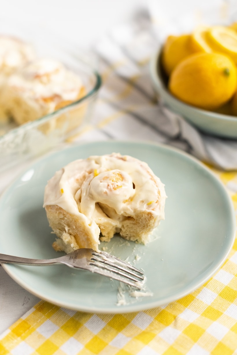 A single lemon bun served on a blue plate, generously topped with lemon cream cheese icing.