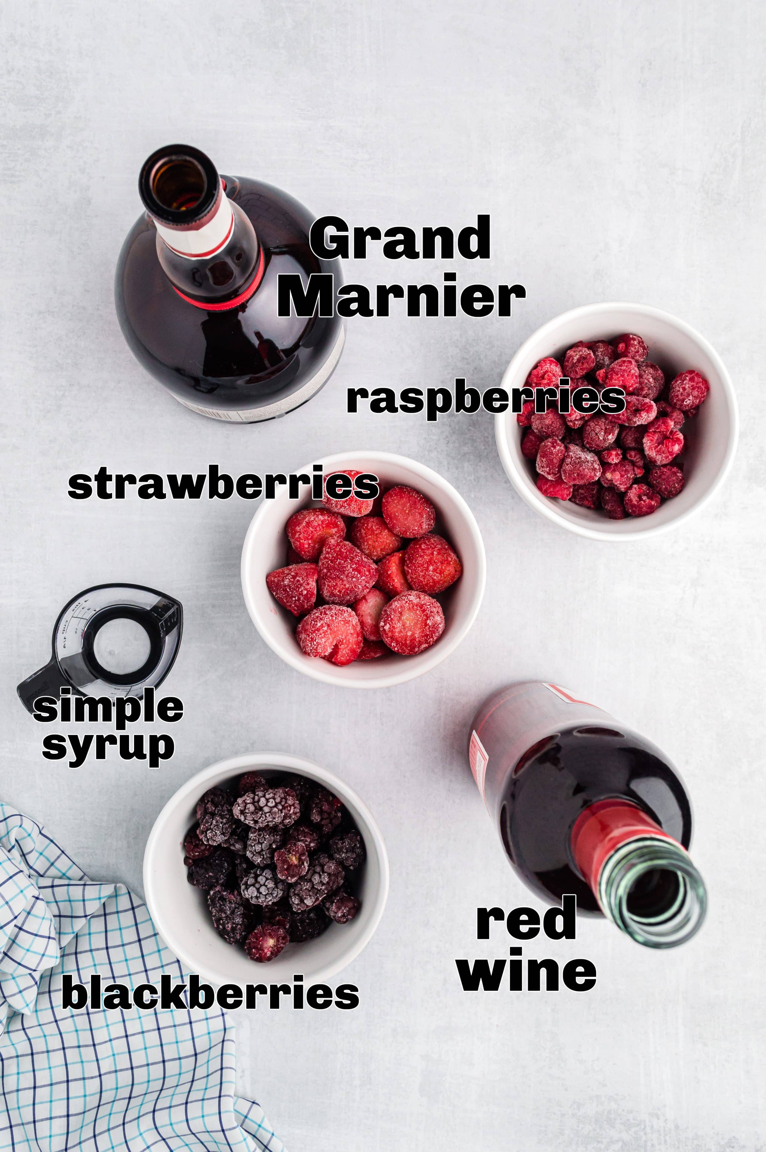 Red wine slushie ingredients: frozen berries, wine, Grand Marnier, and syrup Ingredients for red wine slushie measured out on a surface