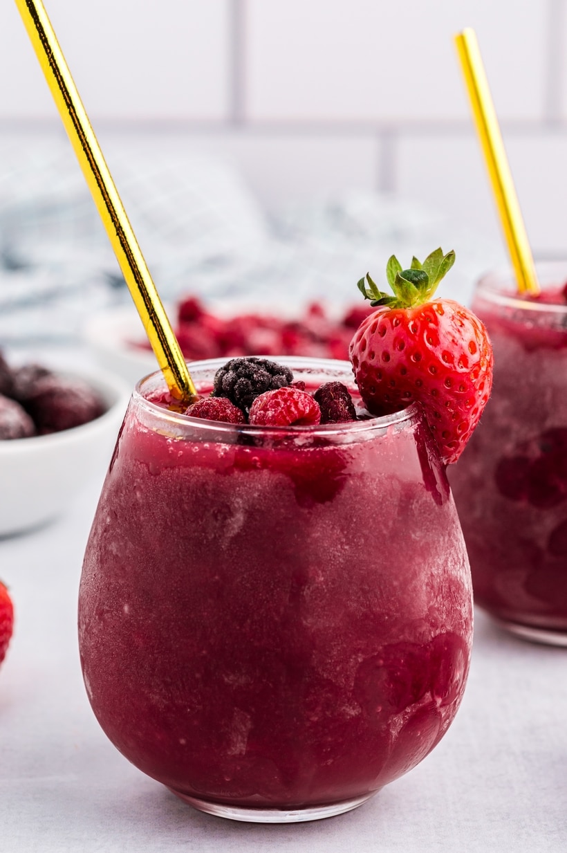 Side angle of red wine slushie with garnish Side view of red wine slushie in stemless glass with strawberry and gold straw