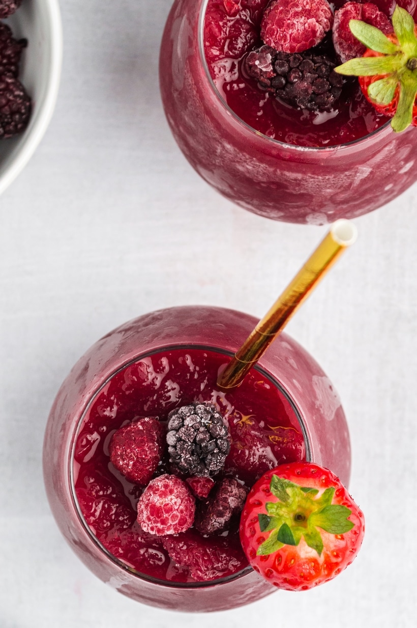 Red wine slushie garnished with frozen berries Overhead shot of red wine slushie in glass with frozen berries and gold straw