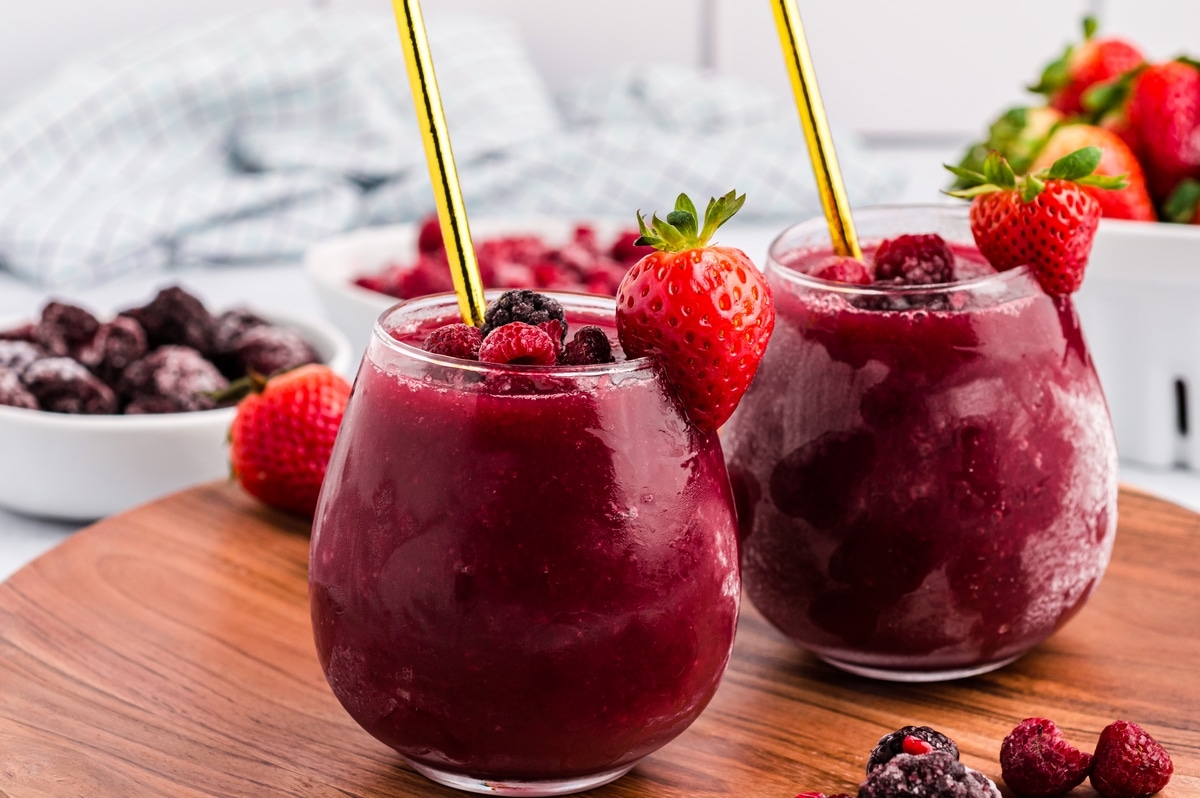 Red wine slushies ready to serve with frozen berry garnish Two glasses of wine slushie on a table with frozen berries around