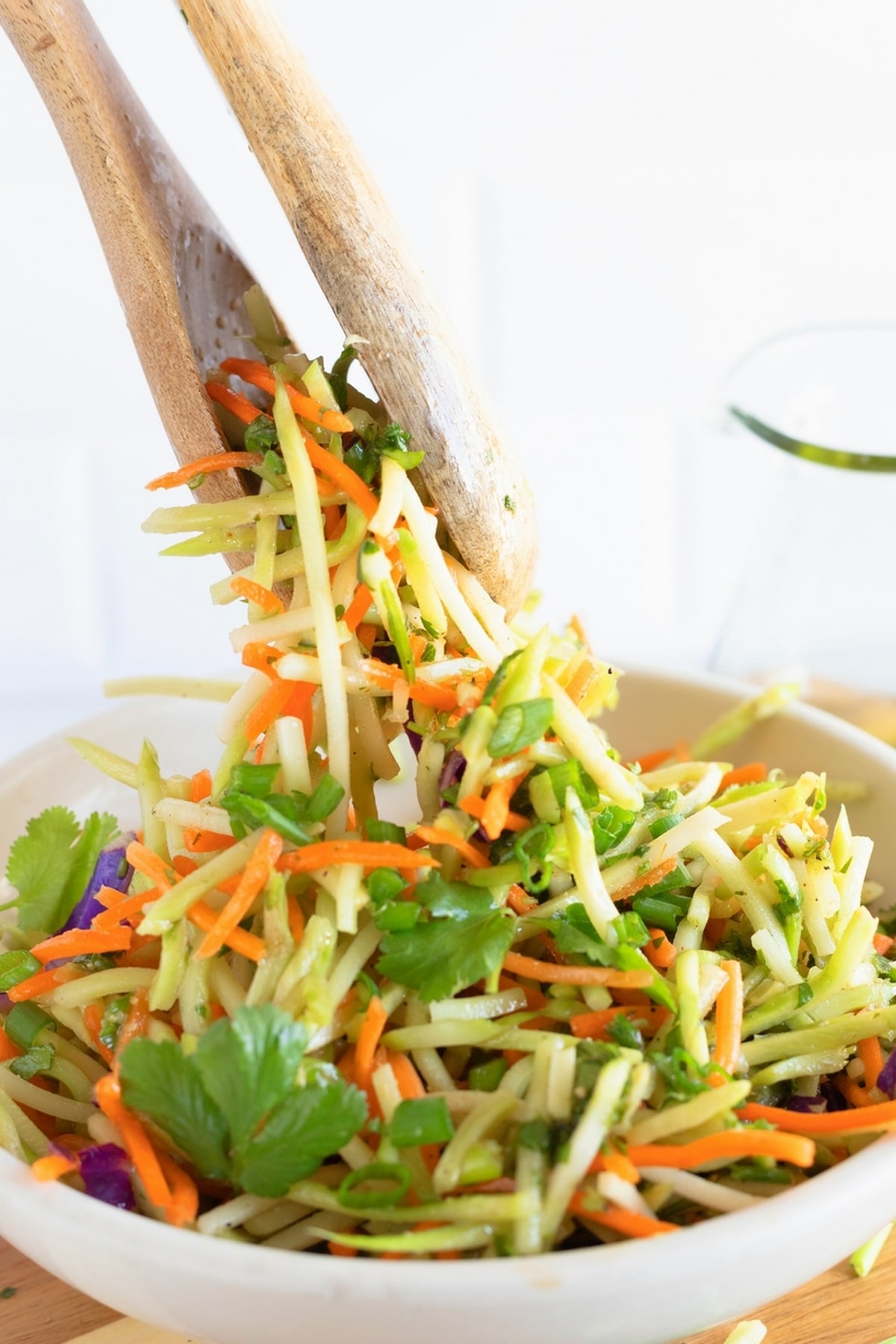 Hand tossing cilantro lime broccoli slaw with dressing in a large bowl.