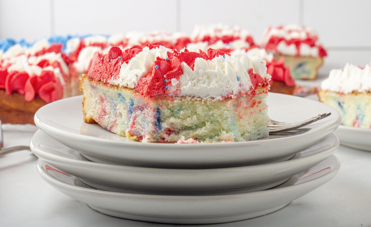 Slice of buttercream flag cake on stacked white plates showing red and blue swirl inside and piped stars on top.