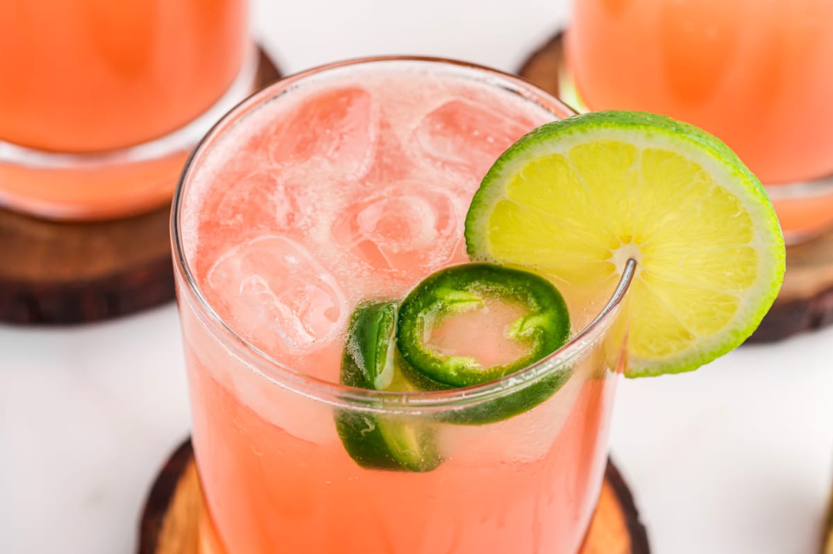Close-up of spicy watermelon jalapeño margarita with ice, lime wheel, and jalapeño slices
