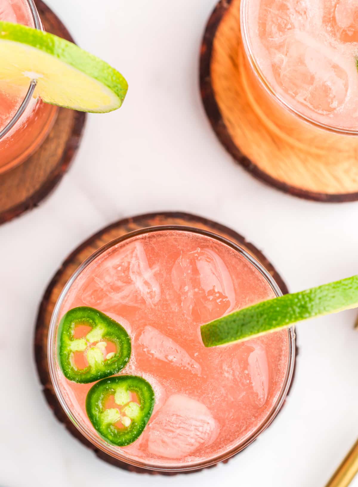 Overhead view of three margaritas with lime and jalapeño on coasters