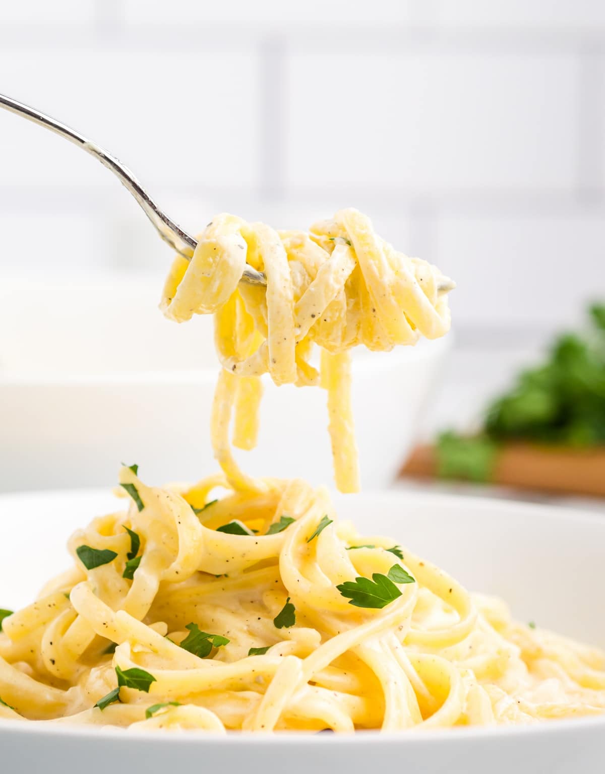 Fork twirling fettuccine over a bowl. A fork twirling a serving of fettuccine over a bowl filled with pasta.