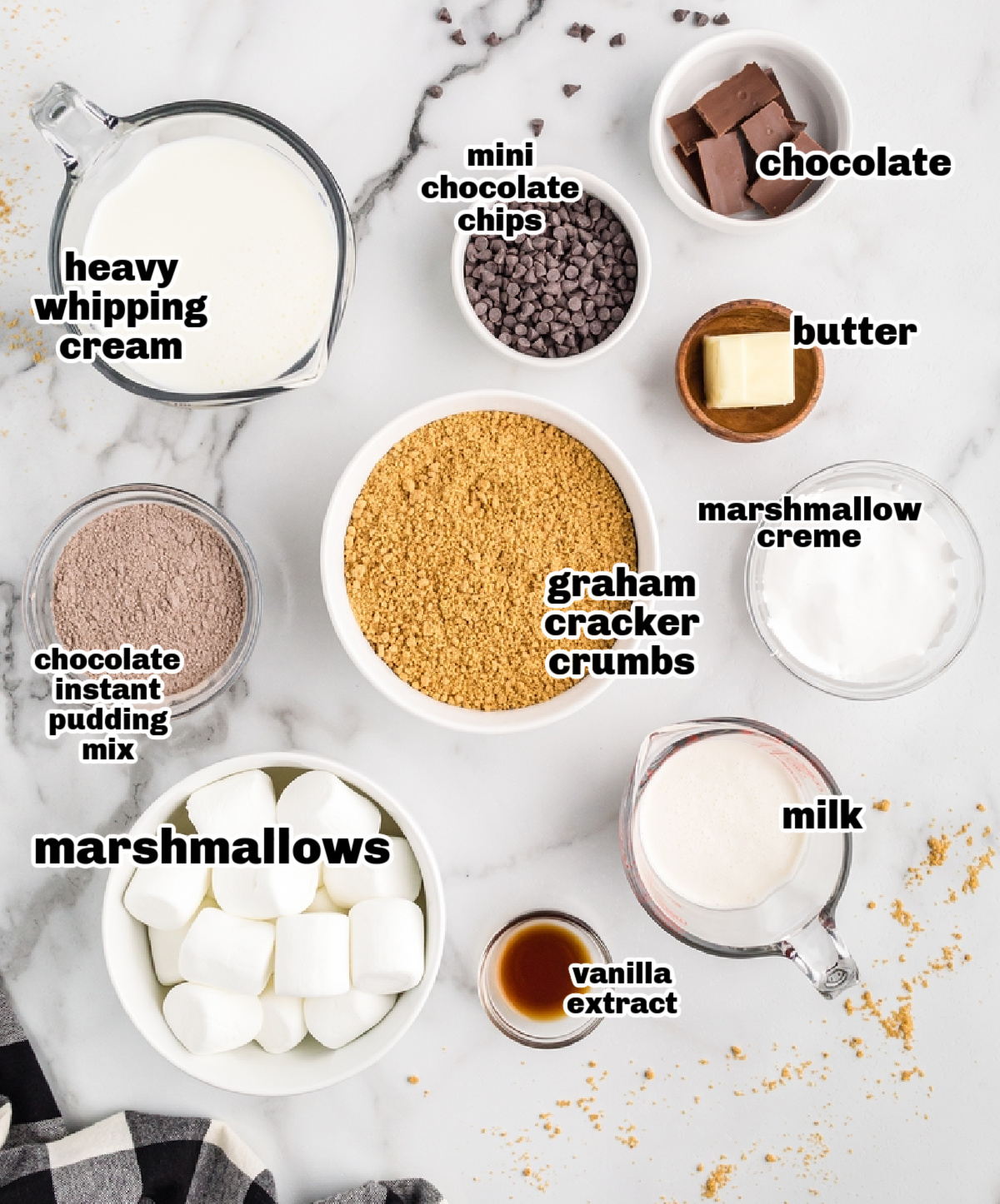 Ingredients for s’mores parfait recipe laid out on marble background Overhead of s’mores parfait ingredients including pudding mix, graham crumbs, chocolate chips, and marshmallows