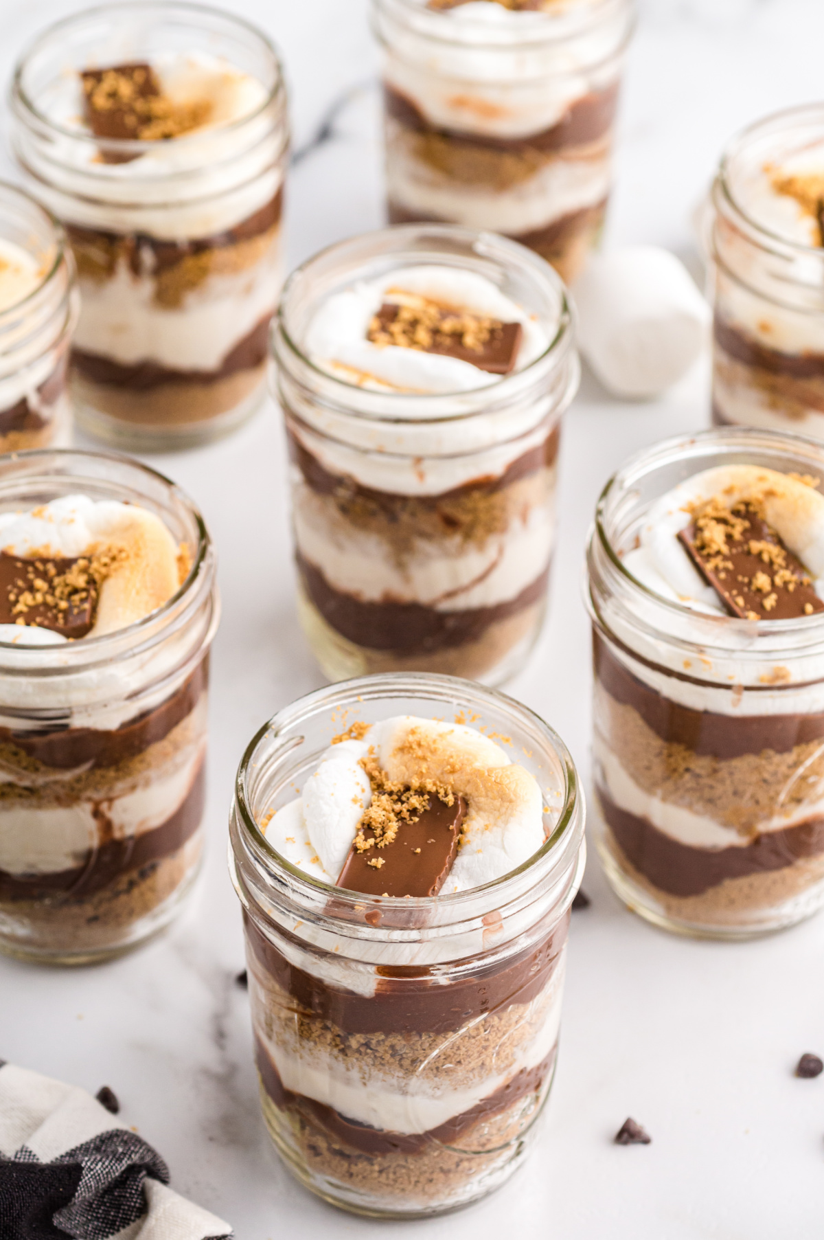 Ingredients for s’mores parfait recipe laid out on marble background Overhead of s’mores parfait ingredients including pudding mix, graham crumbs, chocolate chips, and marshmallows