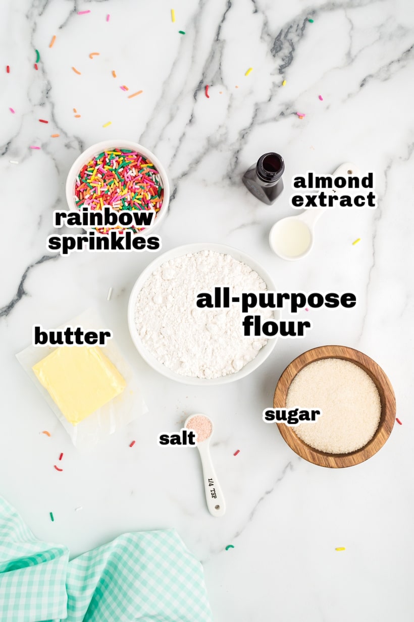Edible Sugar Cookie Dough ingredients A flat lay of all the ingredients needed to make edible sugar cookie dough, including flour, butter, sugar, almond extract, salt, and sprinkles.