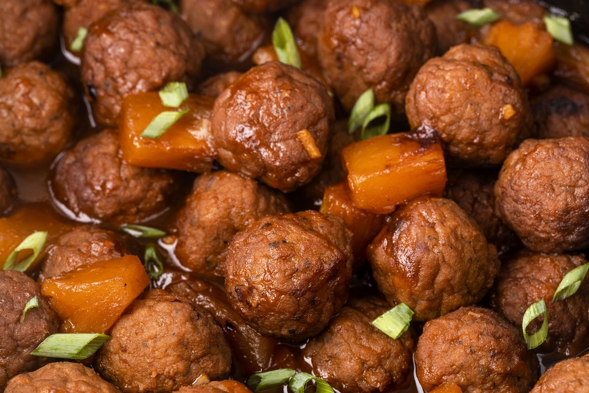 Close-up of flavorful meatballs in a pineapple sauce—great for dinner or appetizers. Close-up of Slow Cooker Hawaiian Meatballs in a white bowl, highlighting their glossy sauce and tender texture.